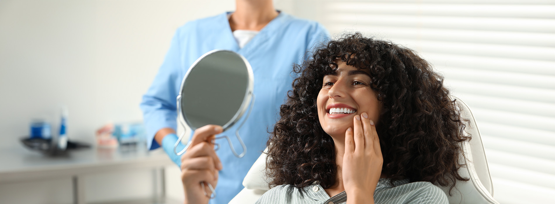The image shows a person sitting in front of a mirror with a hairstylist adjusting their hair while they hold a brush.
