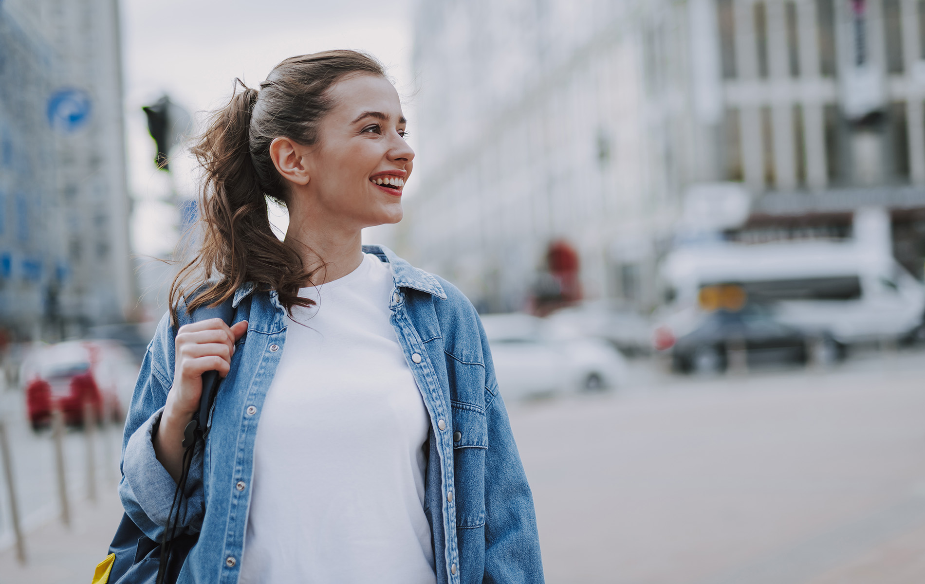The image features a young woman standing on a street corner, smiling at the camera, with a cityscape in the background.