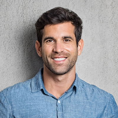 A man with a beard, smiling at the camera, poses against a grey background.