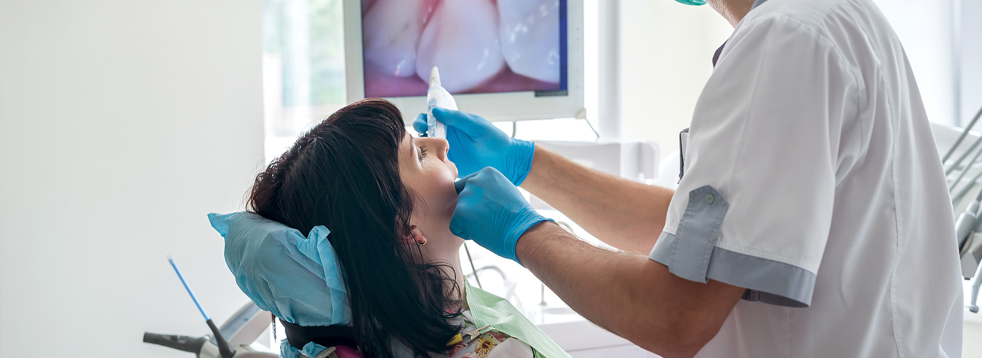 A dental professional performing a procedure on a patient s mouth with a blue light illuminating the area.