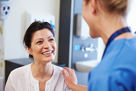 The image shows a woman sitting in a dental chair with a dentist standing beside her, both smiling at each other.