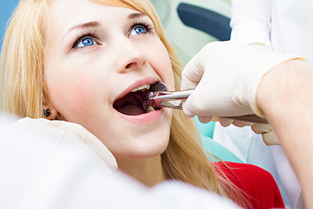The image shows a young woman receiving dental care with her mouth open while sitting in a dental chair, surrounded by dental professionals who appear to be assisting her.