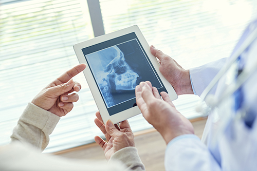 The image shows two people looking at a tablet displaying an X-ray with a healthcare professional s hands holding the device, set against the backdrop of a medical office environment.