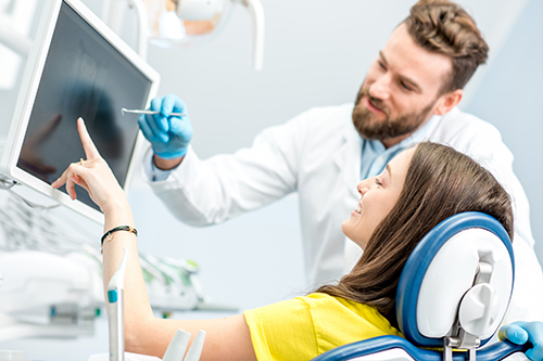 The image shows a man standing next to a woman who is seated in a dental chair, both are in a dental office setting with equipment around them.