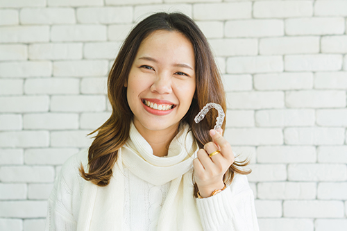 Woman holding a white letter  M  with a smile on her face, standing against a brick wall background.