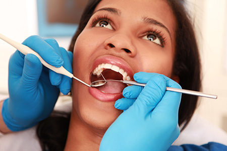 Woman receiving dental care with dental tools being used on her teeth.