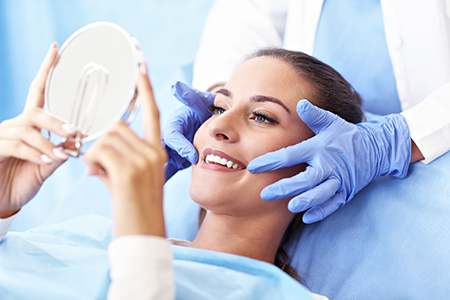 Woman lying on dental chair with mirror held over face.