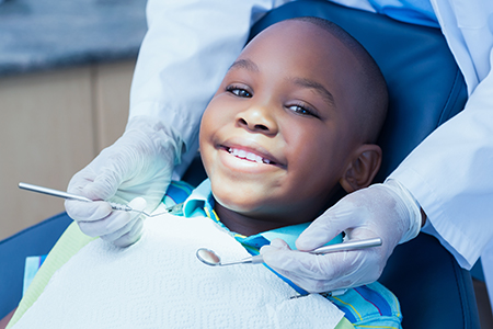 A young boy sitting in a dental chair with a smiling expression, receiving dental care from a dentist.