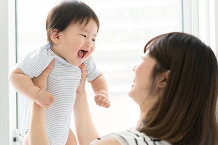 A woman holding a baby with a joyful expression, smiling at the camera.