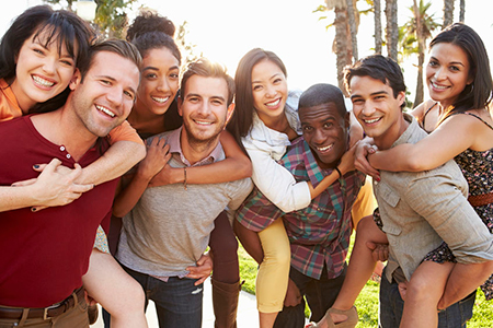 The image shows a group of people posing for a photo with smiles on their faces  they are hugging each other, and the setting appears to be outdoors during daylight.