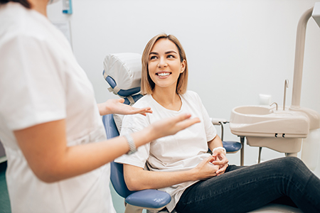 Woman sitting in dental chair smiling at camera with two dental professionals attending to her.