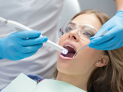 The image depicts a dental professional using an electronic device to clean a patient s teeth during a dental procedure.